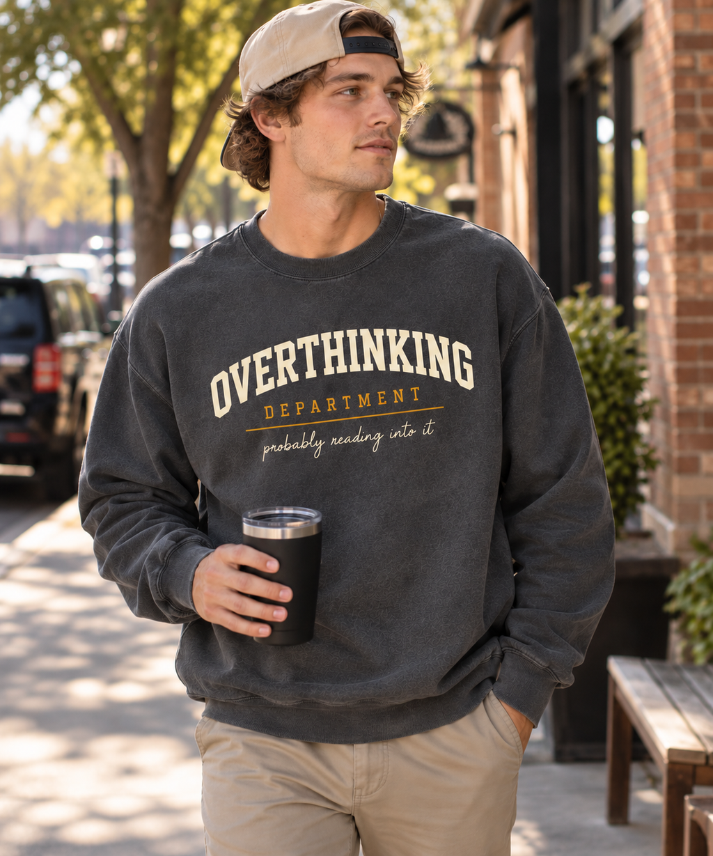 Man wearing the charcoal Overthinking Department crewneck with cream collegiate lettering on a city sidewalk.