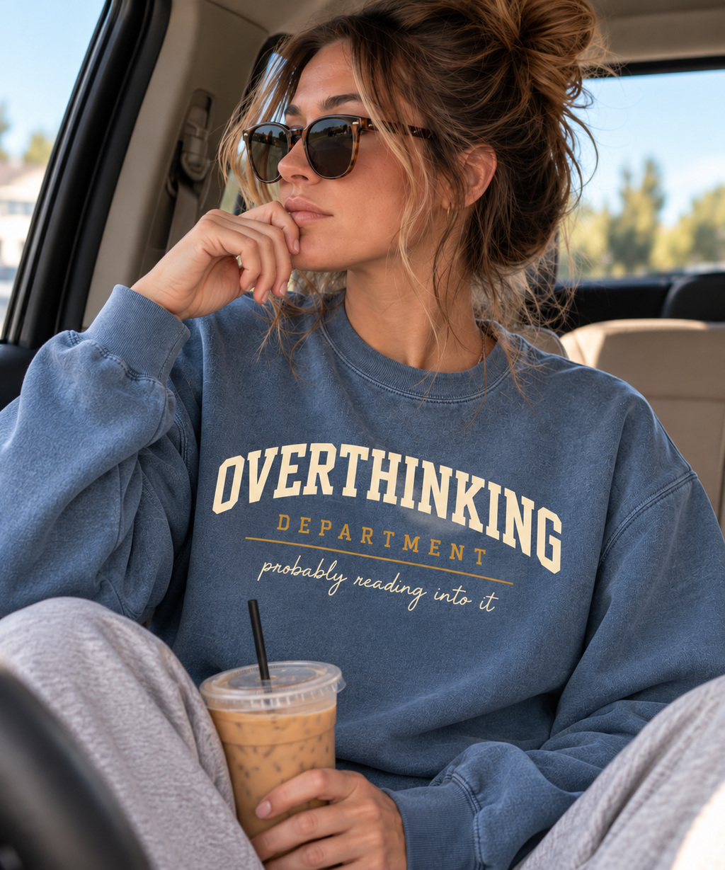 Woman in a car wearing the blue Overthinking Department crewneck and holding an iced coffee.