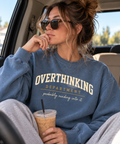 Woman in a car wearing the blue Overthinking Department crewneck and holding an iced coffee.