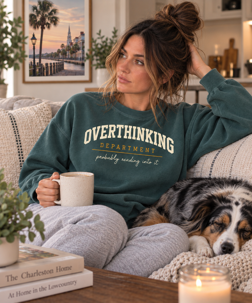 Woman relaxing with a dog and mug while wearing the green Overthinking Department crewneck.